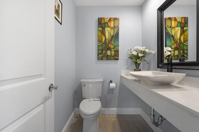 half bath featuring a sink, baseboards, toilet, and wood finished floors