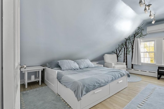 bedroom with track lighting, lofted ceiling, a wall mounted air conditioner, baseboard heating, and light wood-style flooring