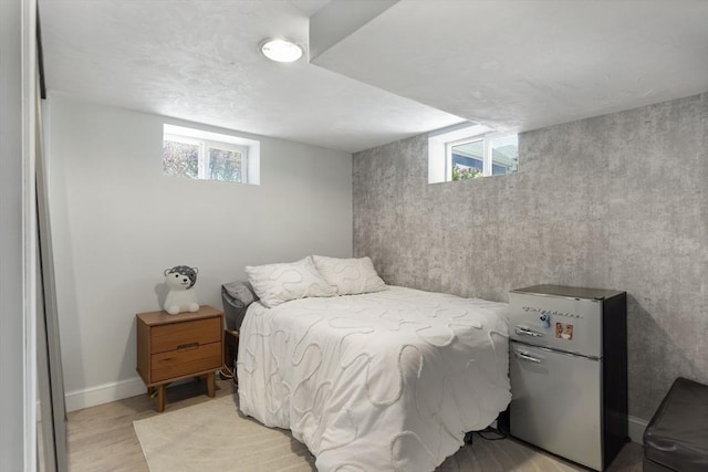 bedroom with baseboards, multiple windows, freestanding refrigerator, and light wood finished floors