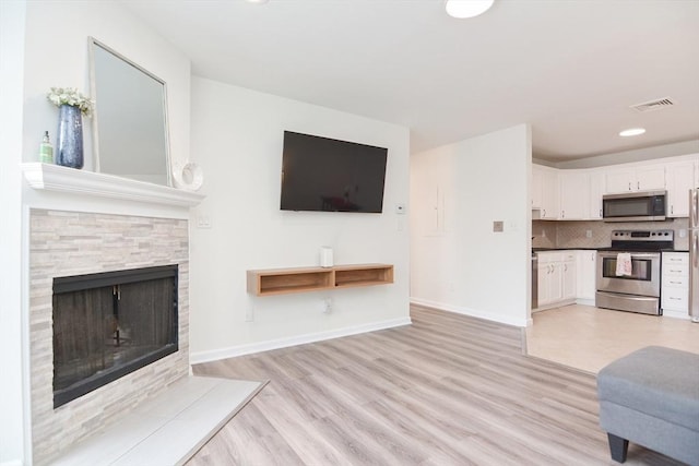 unfurnished living room featuring a stone fireplace and light hardwood / wood-style floors