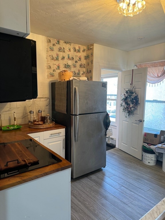 kitchen with tasteful backsplash, wood counters, white cabinetry, light wood-type flooring, and stainless steel fridge