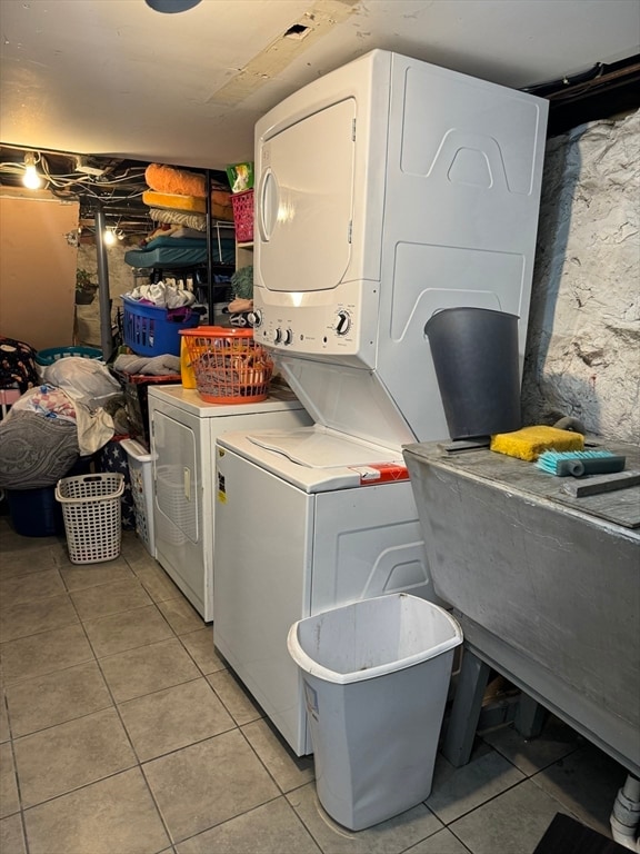 laundry area with stacked washer / drying machine and light tile patterned floors