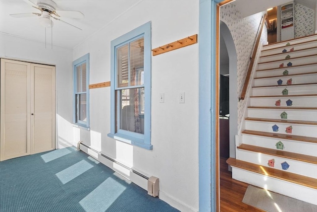 staircase featuring a ceiling fan, arched walkways, and baseboard heating