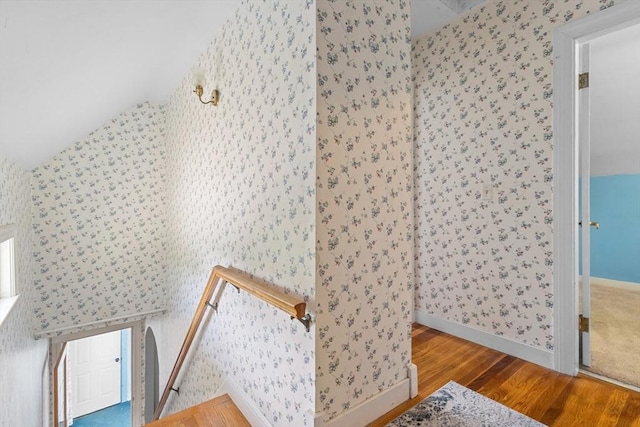 stairway with wallpapered walls, wood finished floors, vaulted ceiling, and baseboards