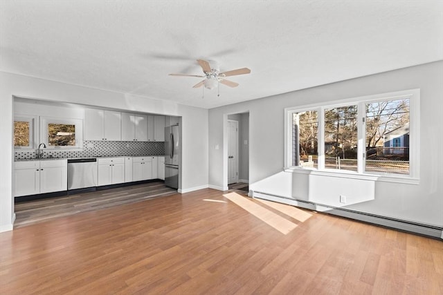 unfurnished living room with wood-type flooring, a baseboard radiator, ceiling fan, and sink