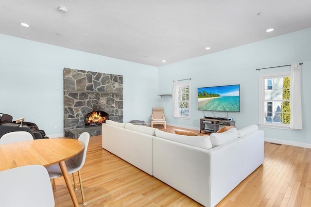 living room with a stone fireplace and light wood-type flooring