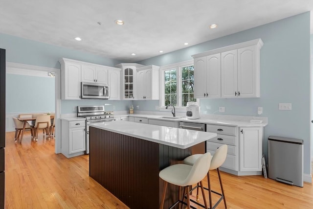 kitchen with appliances with stainless steel finishes, a kitchen island, sink, light hardwood / wood-style floors, and white cabinetry