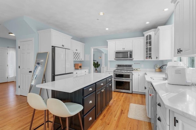 kitchen with sink, light wood-type flooring, appliances with stainless steel finishes, a kitchen island, and white cabinetry