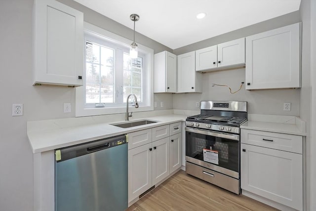 kitchen with pendant lighting, sink, appliances with stainless steel finishes, white cabinetry, and light hardwood / wood-style floors