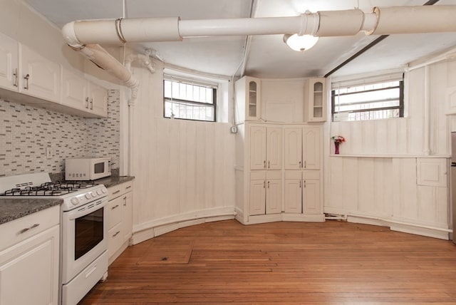 kitchen with wood-type flooring, dark stone counters, white cabinets, tasteful backsplash, and white appliances