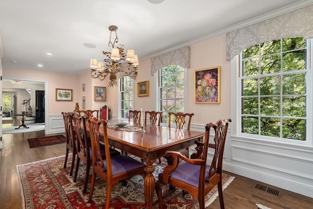 dining room with a chandelier, wainscoting, dark wood-type flooring, crown molding, and a decorative wall