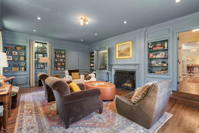 living room featuring crown molding, a decorative wall, wood finished floors, a high end fireplace, and built in features