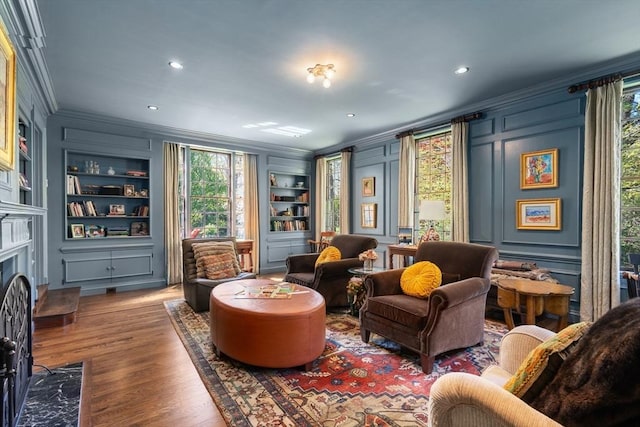 living area with ornamental molding, built in shelves, a decorative wall, plenty of natural light, and wood finished floors