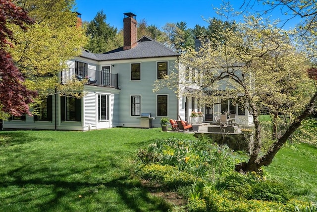 back of house featuring a balcony, a lawn, a patio area, and a chimney