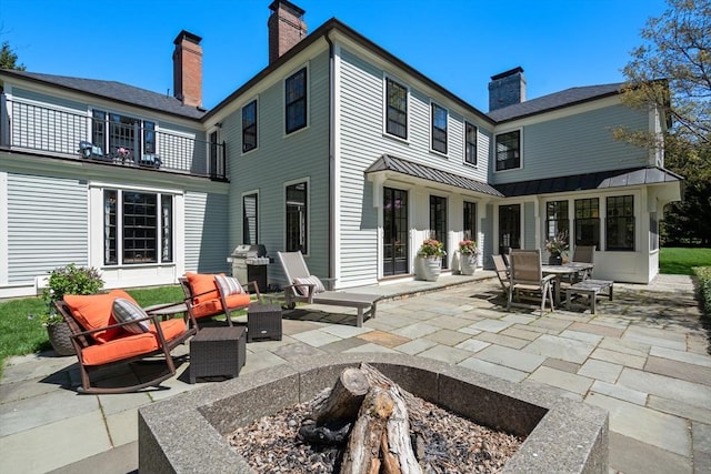 back of house with a chimney, a balcony, a patio area, and a standing seam roof