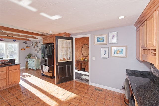 kitchen featuring light brown cabinets, beamed ceiling, dark stone countertops, black refrigerator, and light tile patterned flooring