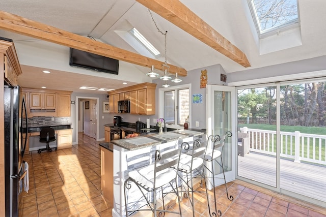 kitchen with pendant lighting, black appliances, vaulted ceiling with skylight, dark stone countertops, and kitchen peninsula