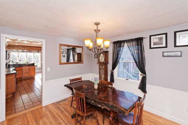 dining space featuring light hardwood / wood-style flooring, a textured ceiling, and a notable chandelier