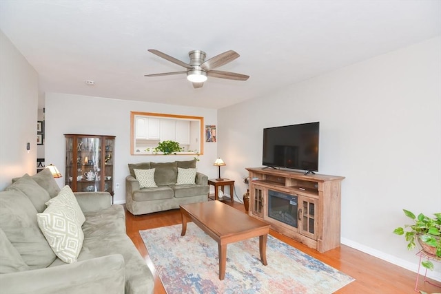 living room with baseboards, light wood-type flooring, and ceiling fan