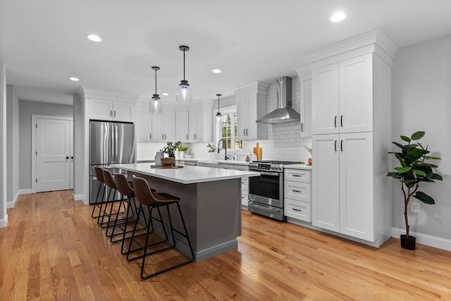 kitchen with wall chimney range hood, decorative backsplash, appliances with stainless steel finishes, decorative light fixtures, and white cabinetry