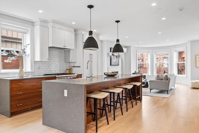 kitchen with light wood finished floors, white cabinets, a kitchen breakfast bar, stainless steel gas stovetop, and backsplash