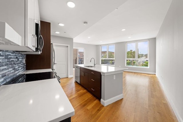 kitchen featuring dishwasher, light hardwood / wood-style floors, dark brown cabinets, sink, and a kitchen island with sink