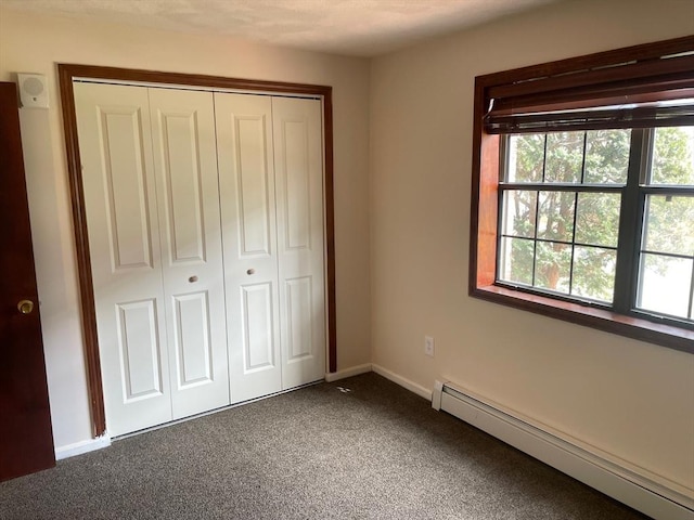 unfurnished bedroom featuring a baseboard heating unit, dark carpet, and a closet