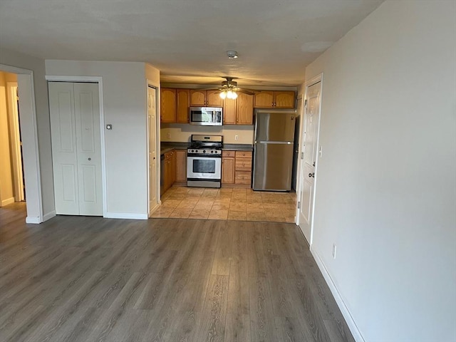 kitchen featuring brown cabinets, light wood finished floors, stainless steel appliances, baseboards, and ceiling fan