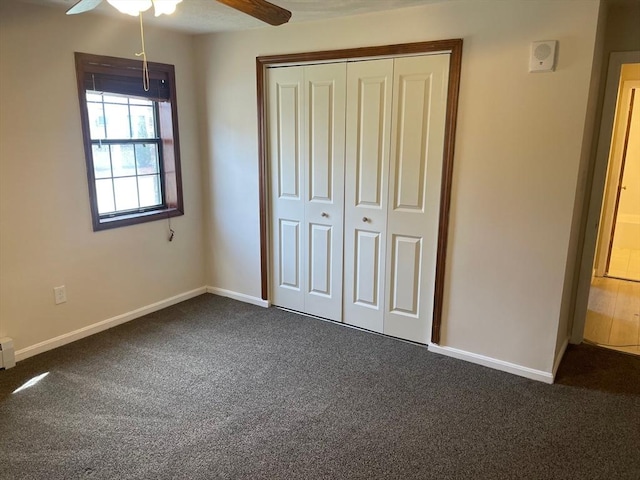 unfurnished bedroom with dark colored carpet, baseboards, a closet, and ceiling fan