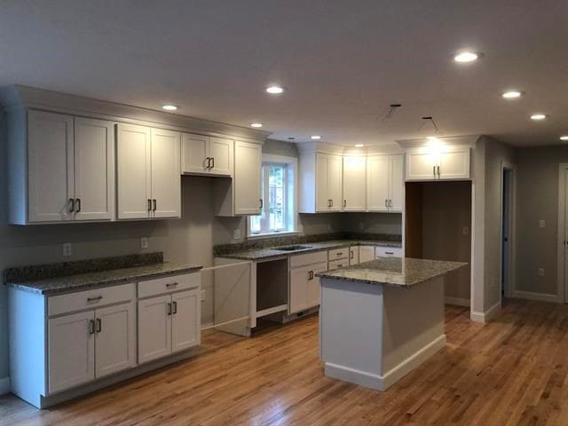 kitchen featuring a kitchen island, white cabinetry, sink, dark stone countertops, and light hardwood / wood-style flooring