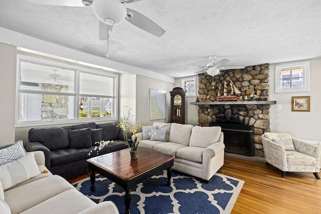 living room with a textured ceiling, wood-type flooring, and a stone fireplace