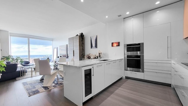 kitchen with stainless steel double oven, white cabinetry, kitchen peninsula, a water view, and expansive windows