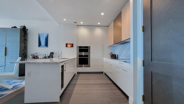 kitchen featuring kitchen peninsula, double oven, sink, white cabinets, and light stone countertops