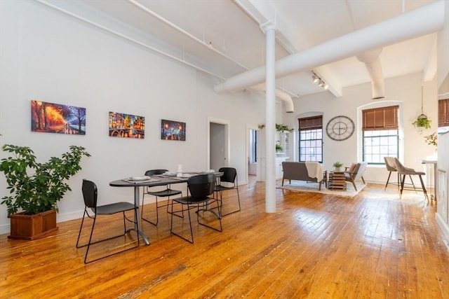 dining space featuring beamed ceiling, hardwood / wood-style floors, decorative columns, and a high ceiling