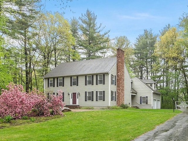 colonial inspired home featuring a chimney, a front yard, driveway, and a garage