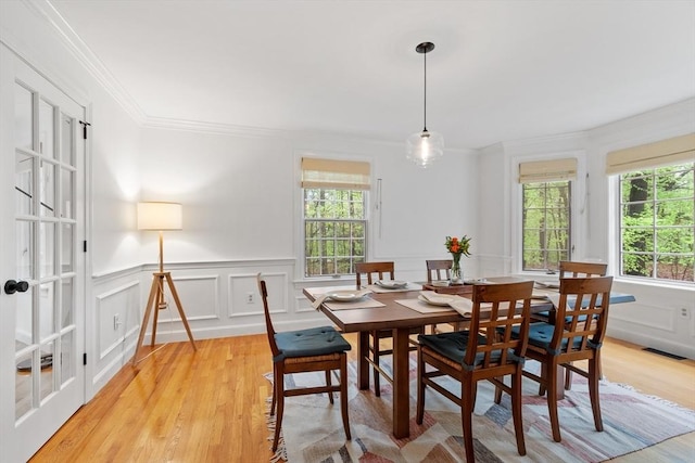 dining area featuring ornamental molding, plenty of natural light, light wood-style flooring, a decorative wall, and wainscoting