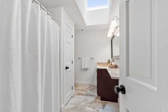 full bathroom featuring a skylight, marble finish flooring, vanity, and baseboards