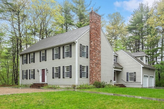 colonial inspired home with a chimney, a front yard, a garage, and roof with shingles