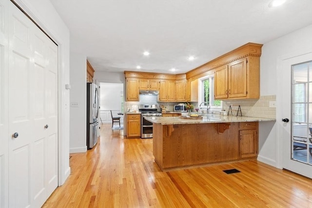 kitchen with appliances with stainless steel finishes, under cabinet range hood, light wood finished floors, a peninsula, and recessed lighting