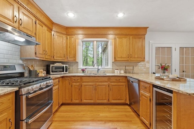 kitchen with appliances with stainless steel finishes, wine cooler, a sink, under cabinet range hood, and a peninsula