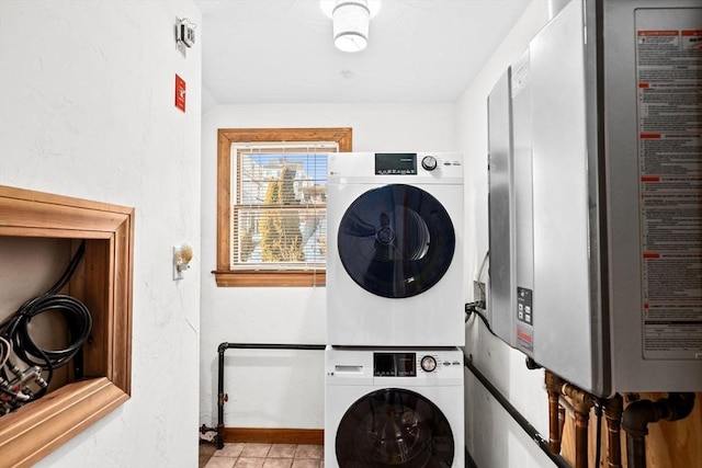 laundry room featuring light tile patterned floors, stacked washer and dryer, tankless water heater, laundry area, and baseboards