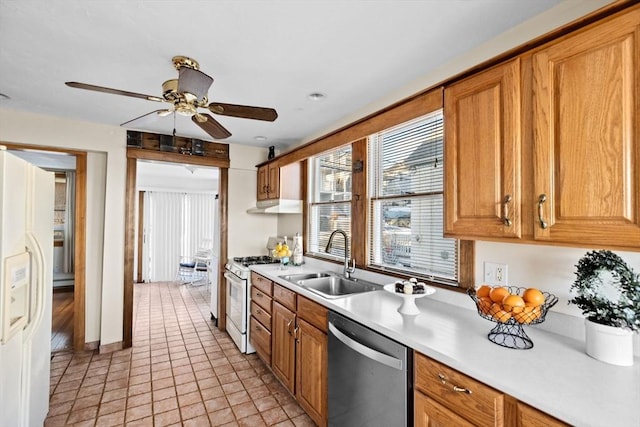 kitchen featuring under cabinet range hood, white appliances, a sink, light countertops, and brown cabinetry