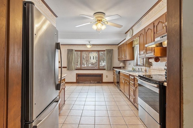 kitchen featuring under cabinet range hood, stainless steel appliances, a sink, radiator, and wallpapered walls