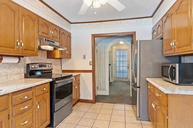 kitchen featuring brown cabinetry, ornamental molding, stainless steel appliances, light countertops, and under cabinet range hood