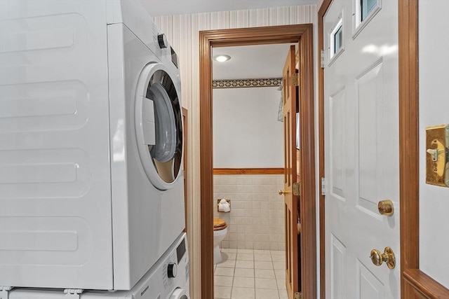 washroom with stacked washer and dryer, light tile patterned floors, and tile walls