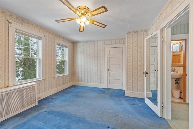 carpeted spare room with baseboards, radiator, a ceiling fan, and wallpapered walls