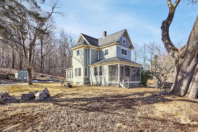 view of front facade featuring an outbuilding, a shed, a sunroom, a shingled roof, and a chimney