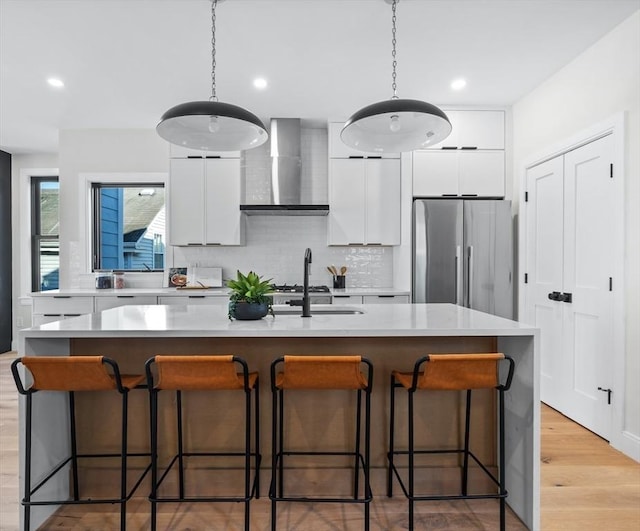 kitchen with freestanding refrigerator, light countertops, wall chimney range hood, white cabinetry, and a sink