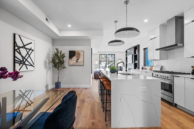 kitchen with modern cabinets, a sink, wall chimney range hood, and high end stainless steel range