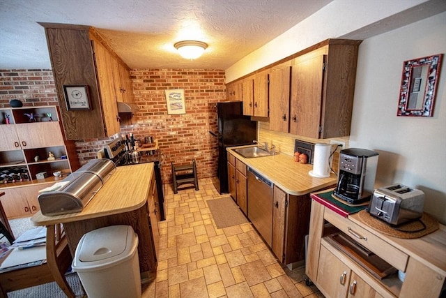 kitchen with appliances with stainless steel finishes, stone finish floor, a sink, a textured ceiling, and brick wall